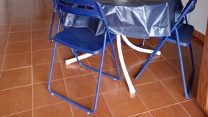 Ein Essbereich mit einem runden Tisch, der mit einer schwarzen Tischdecke bedeckt ist, umgeben von blauen Stühlen. Auf dem Tisch steht eine weiße Vase. Der Raum hat einen gefliesten Boden und eine beigefarbene Couch im Hintergrund.