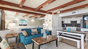 A modern living room with a blue sofa, a wooden coffee table, and a kitchen in the background.