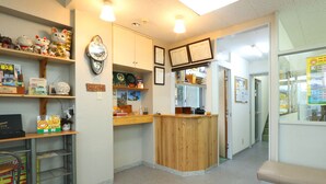 Un espace d’accueil avec un comptoir en bois, des étagères remplies de divers objets, une horloge et des certificats encadrés accrochés au mur.