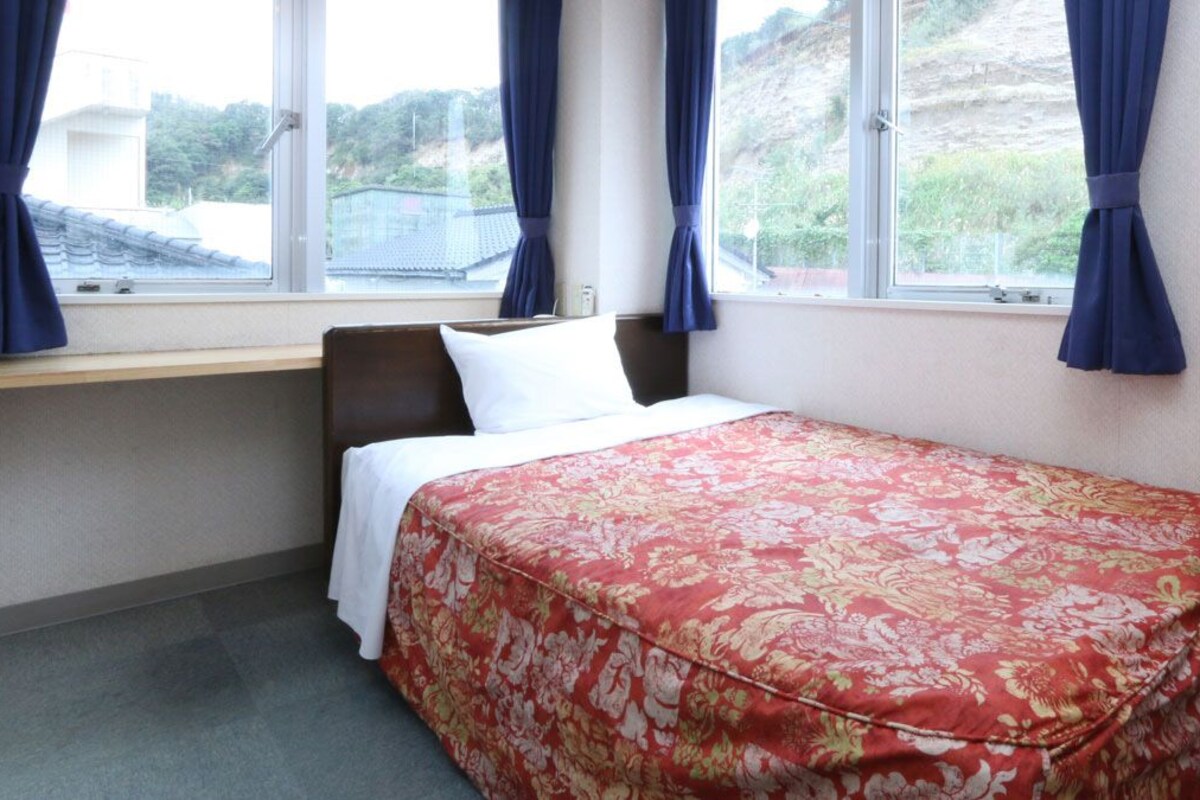 A room with a bed, a window with curtains, and a view of greenery outside.
