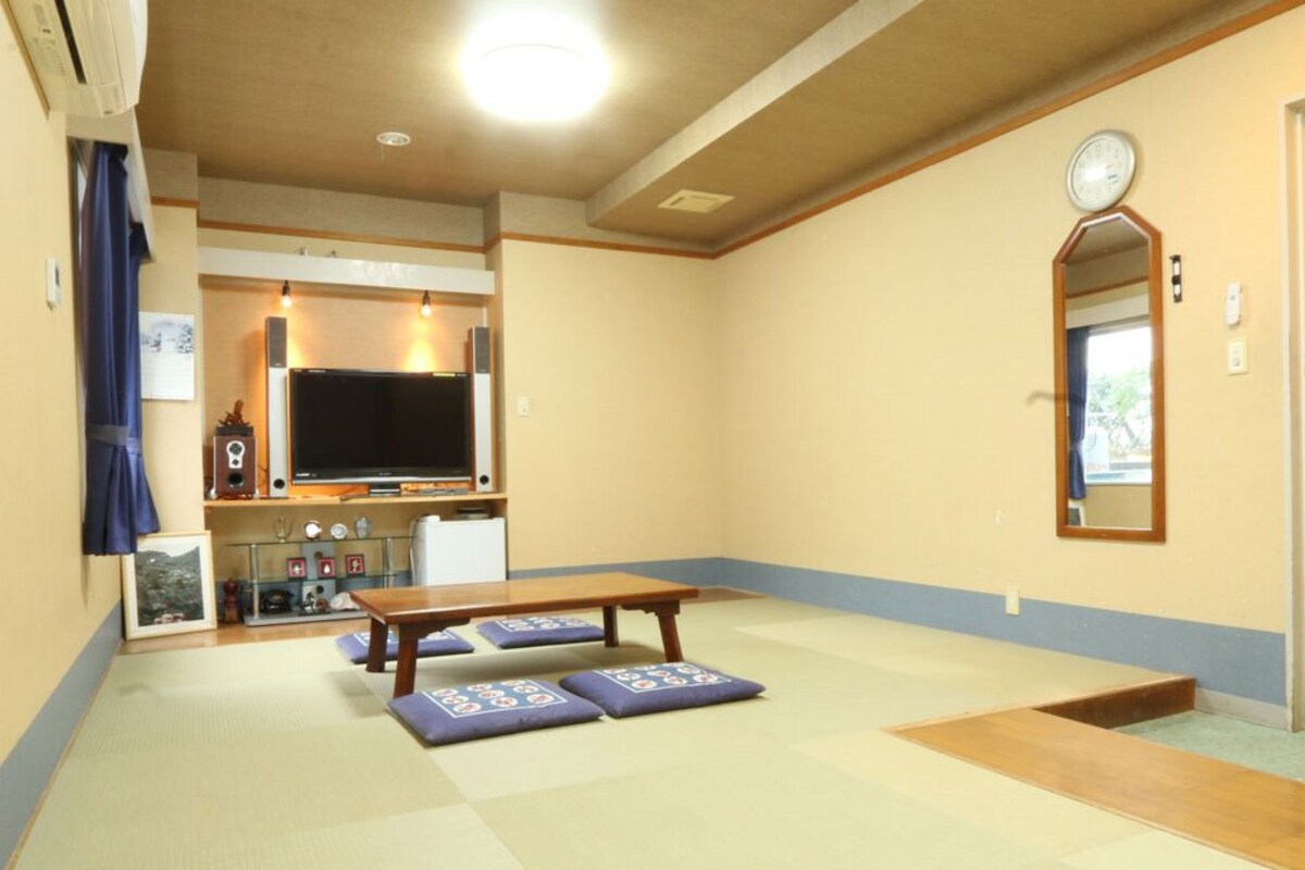 Una habitación con esteras de tatami, una televisión, una mesa de madera y un espejo en la pared.
