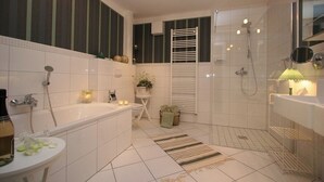 A modern bathroom with a bathtub, shower, and sink. There are towels and a small plant on the floor. - Hof Eckhorst, Apartment Sonnenschein (Güby)