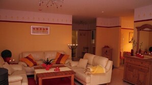 A living room with a beige sofa, a wooden coffee table, and a red rug. There is a wooden cabinet and a mirror on the right side. - Hof Eckhorst, Apartment Sonnenschein (Güby)