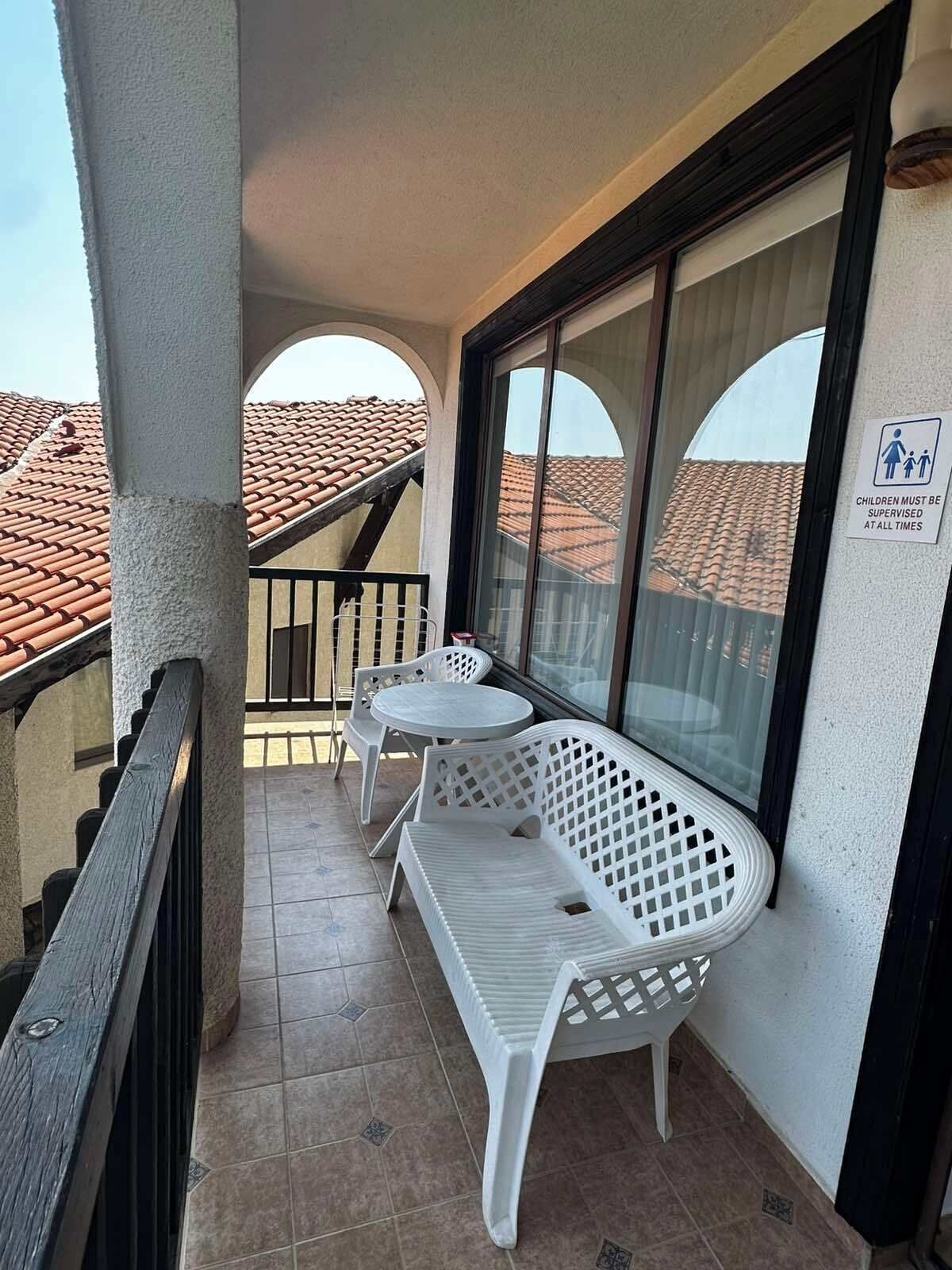 Un balcón con mobiliario blanco de plástico, una puerta de cristal y un letrero que indica que se debe vigilar a los niños.