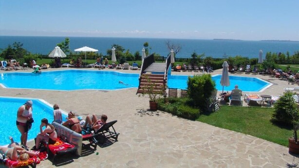 Un espace piscine comprenant deux piscines, des chaises longues, des parasols et une vue sur la mer.