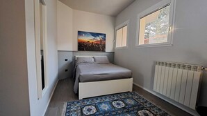 A small, modern bedroom with a bed, a cityscape painting, a window, and a radiator. - Apartment MXP Milan Como Laghi free private parking (Castellanza)