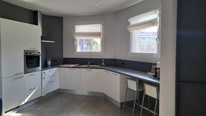 A modern kitchen with white cabinets, a built-in oven, a sink, and two windows with blinds. - Apartment MXP Milan Como Laghi free private parking (Castellanza)
