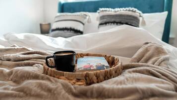 A bed with a coffee cup and a book on a woven tray.