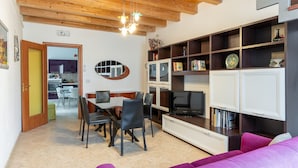 A modern living room with a dining area, wooden ceiling, and built-in shelving with books and decorative items. - A 100 Metri da Piazza Duomo di Ortigia by Wonderful Italy (Syracuse)