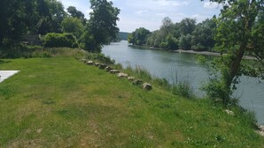 Uma área gramada com rio, árvores e um caminho de pedra.