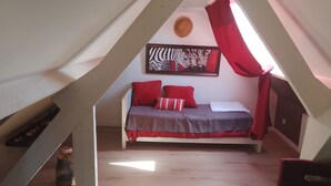 Quarto em estilo loft com teto inclinado, cama com roupa de cama vermelha, pintura de zebra na parede e um vaso rústico no chão.