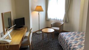 A hotel room with a bed, a desk with a computer and phone, a chair, a lamp, and a window with curtains. - Espoir Iwate (Morioka)