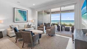 A modern living room with a large window overlooking the beach, furnished with a sofa, chairs, and a coffee table. - Henderson Beach Villa #2 (Destin)