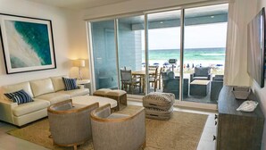 A spacious living room with a large sliding glass door leading to a balcony with a view of the ocean. There is a sofa, two armchairs, and a coffee table. - Henderson Beach Villa #2 (Destin)