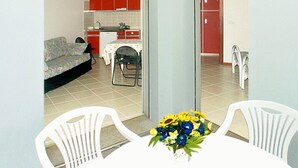 A compact living space with a kitchenette, a sofa, a dining table with chairs, and a small kitchen area with red cabinets. - Cozy Apartment Near the Beach With Parking Space Included (Lignano Sabbiadoro)