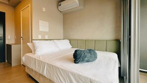 Une chambre d’hôtel avec un lit, une tête de lit verte, un appareil de climatisation et une porte.