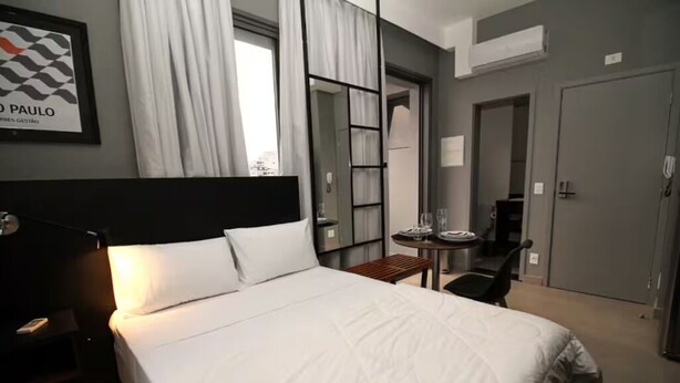 Une chambre d’hôtel avec un grand lit, une table de chevet avec une lampe, une petite table avec une chaise et un tableau encadré au mur.