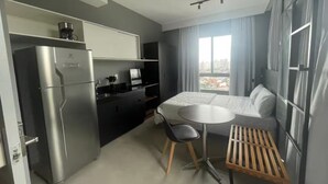 Une chambre d’hôtel compacte comprenant un coin cuisine, un lit, une petite table à manger et une fenêtre avec des rideaux.