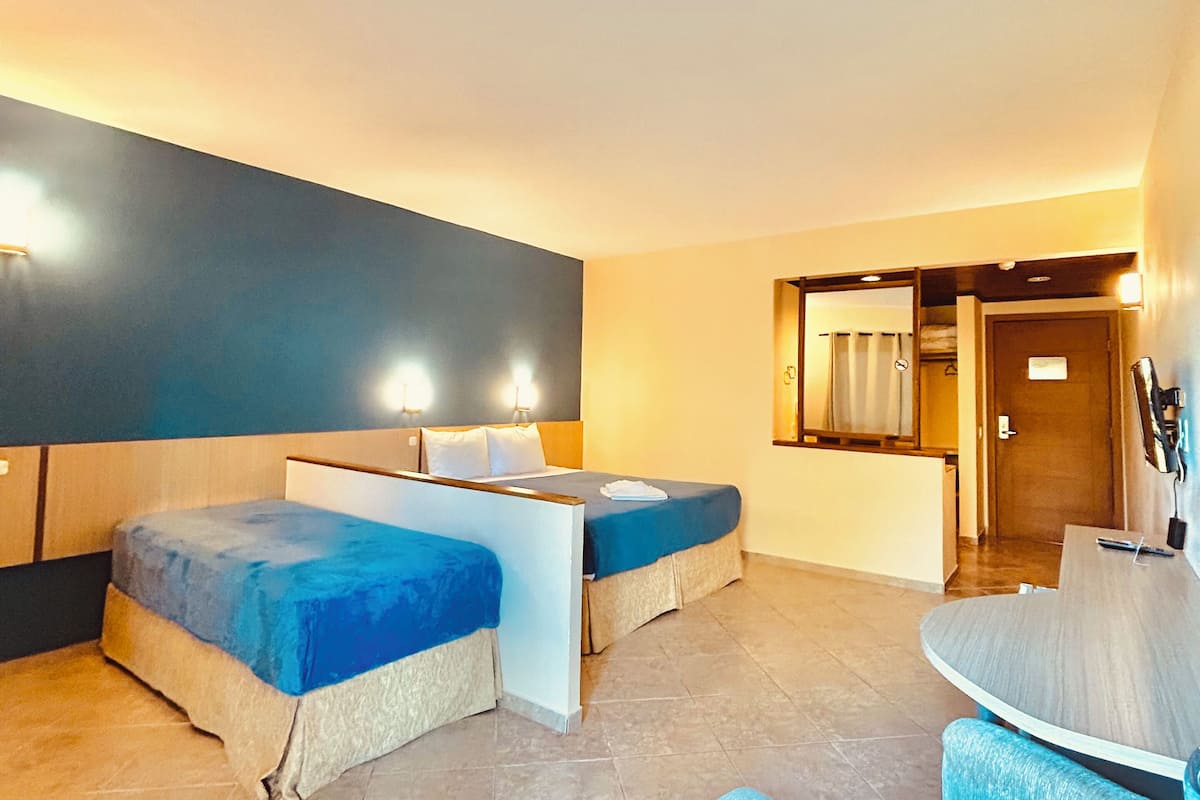 A hotel room with two beds, a small table, and a seating area.
