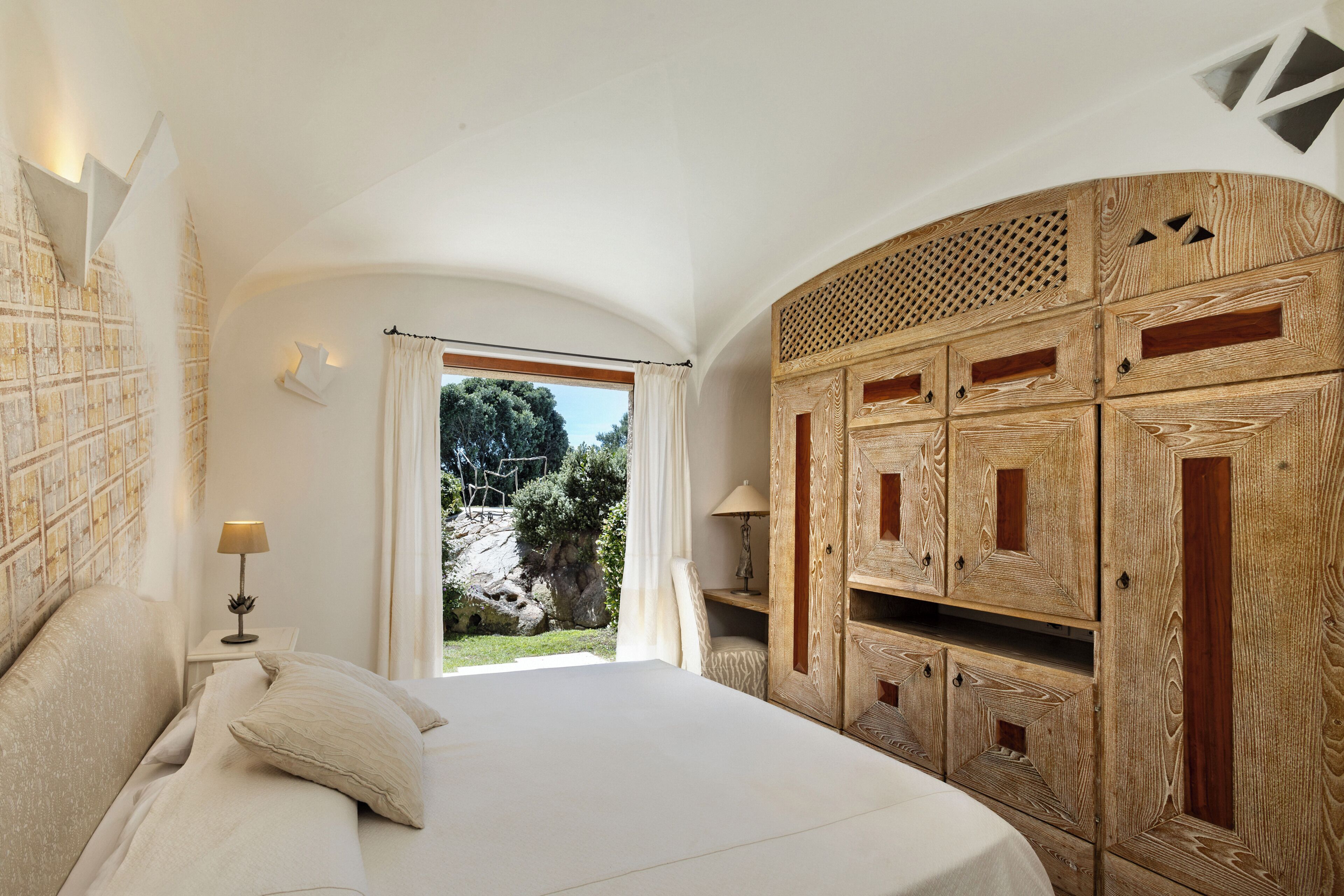 A bedroom with a bed, a nightstand, a lamp, and a wooden wardrobe.