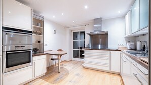 A modern kitchen with stainless steel appliances, white cabinetry, and a wooden dining table. - LIBORIA Alpenblick country house (Uffing am Staffelsee)