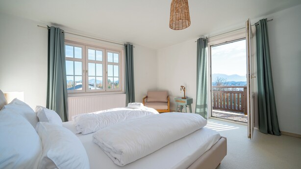 A bedroom with a large bed, a chair, a small table, and a view of the outdoors through a sliding door. - LIBORIA Alpenblick country house (Uffing am Staffelsee)