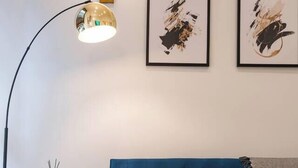 Un salón moderno con un sofá azul, una lámpara de pie redonda y dos cuadros abstractos enmarcados en la pared.