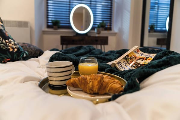 A neatly made breakfast on a bed with a tray, a striped mug, a glass of orange juice, a croissant, and a magazine.