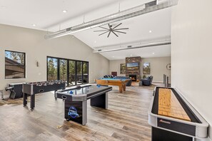 A spacious indoor recreational area with multiple foosball tables, a pool table, and a shuffleboard table.