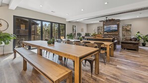 Een ruime zithoek met een grote houten tafel en banken, een open haard, en een televisie bevestigd aan een metselwerk muur.