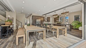 Een ruime keuken met houten tafels en stoelen, een groot eiland en moderne apparatuur.