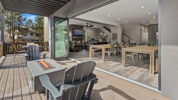 Een modern terras buiten met een vuurkuil, zitplaatsen en uitzicht op het interieur.