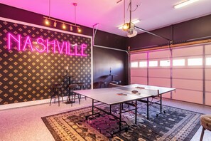 Una stanza con un tavolo da ping pong, un neon con la scritta "NASHVILLE" e un muro decorato.