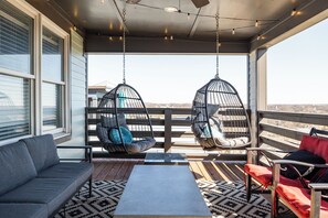 Un balcone con un divano grigio, due poltrone sospese con cuscini, un tavolino e un tappeto decorato.