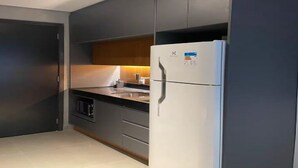 A modern kitchen with dark cabinetry, a stainless steel refrigerator, and a microwave. - OSCAR FREIRE 614 (Pinheiros São Paulo)