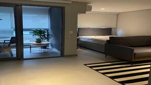A modern hotel room with a bed, a sofa, a small table with a plant, and a view through a sliding door to a balcony. - OSCAR FREIRE 614 (Pinheiros São Paulo)