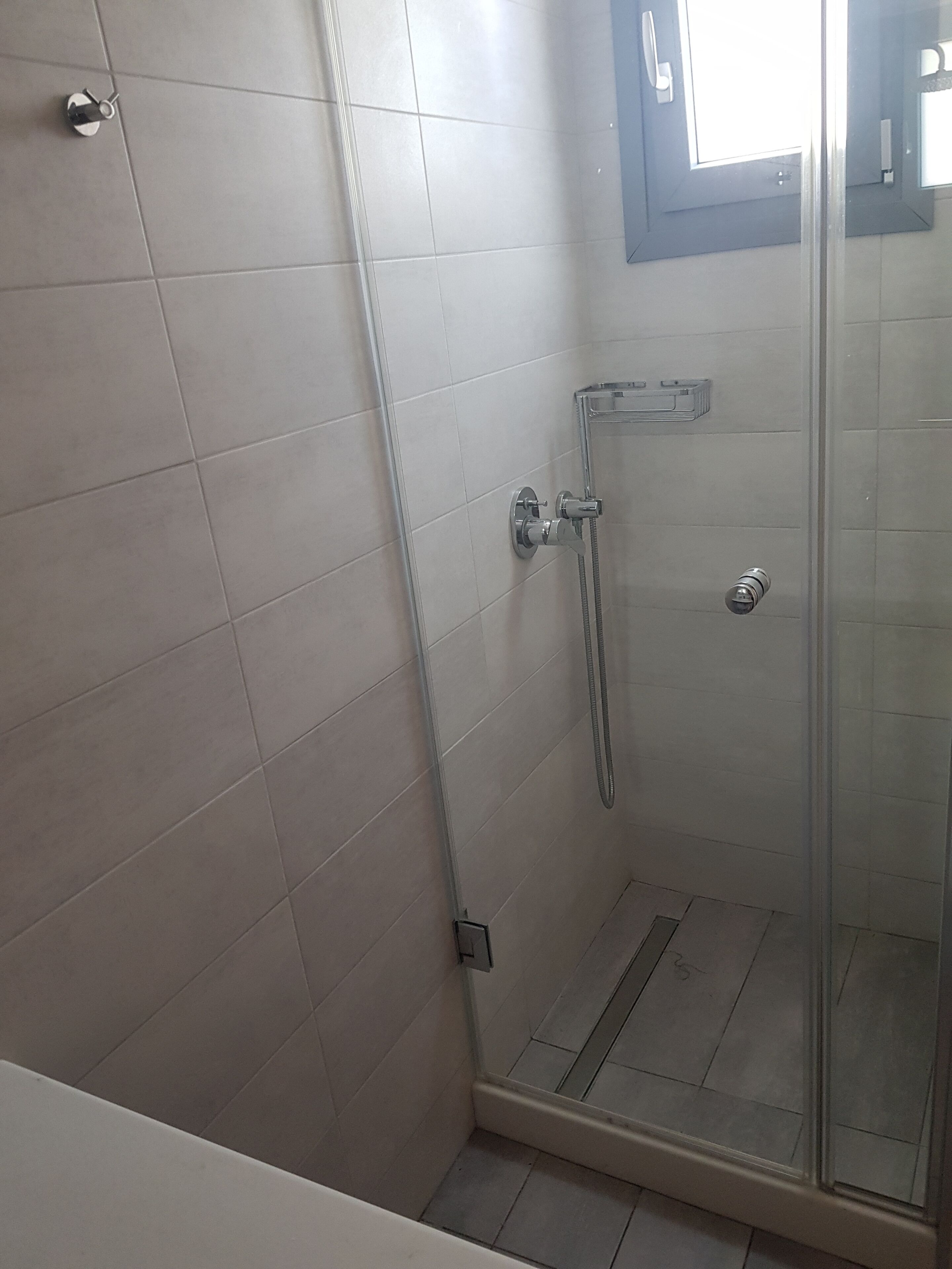 A glass-enclosed shower area with a handheld showerhead and a wall-mounted faucet.