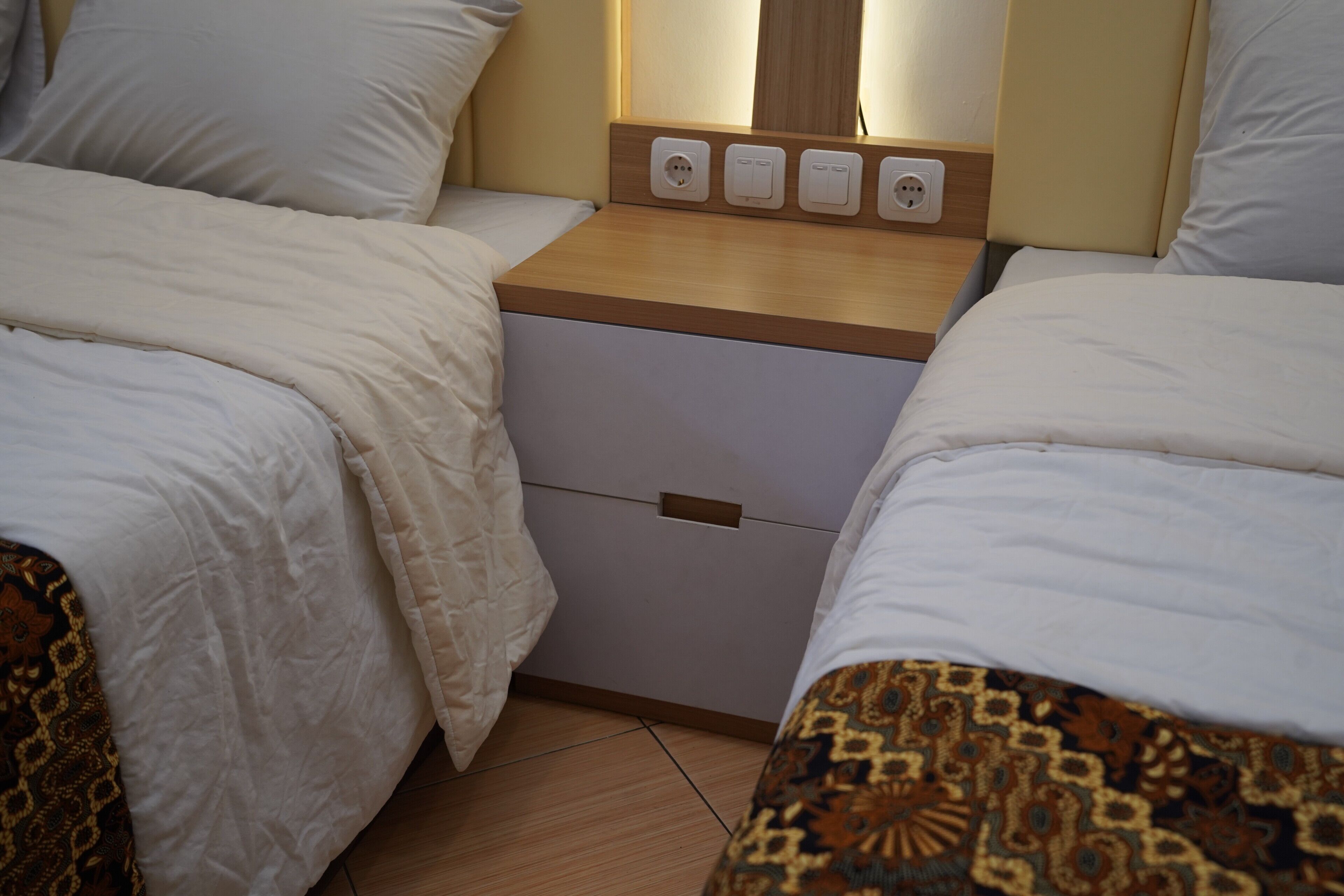 Ein Schlafzimmer mit zwei Betten, einem Nachttisch aus Holz mit Schublade und einer Steckdose.