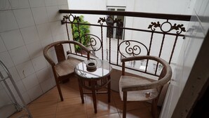 A small balcony with two wooden chairs and a round table, featuring a metal railing and a view of greenery outside. - Grha Somaya (Yogyakarta)