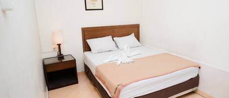 A neatly made bed with white and brown bedding, a wooden headboard, and a small bedside table with a lamp.