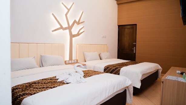 A hotel room with two beds, a wooden door, and a wall-mounted tree light. - Grha Somaya (Yogyakarta)