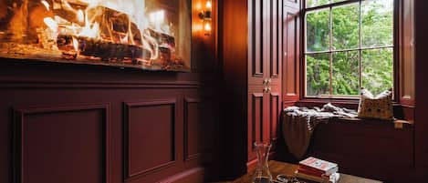 A cozy room with a fireplace, a window with a view of greenery, and a wooden table with a tray.