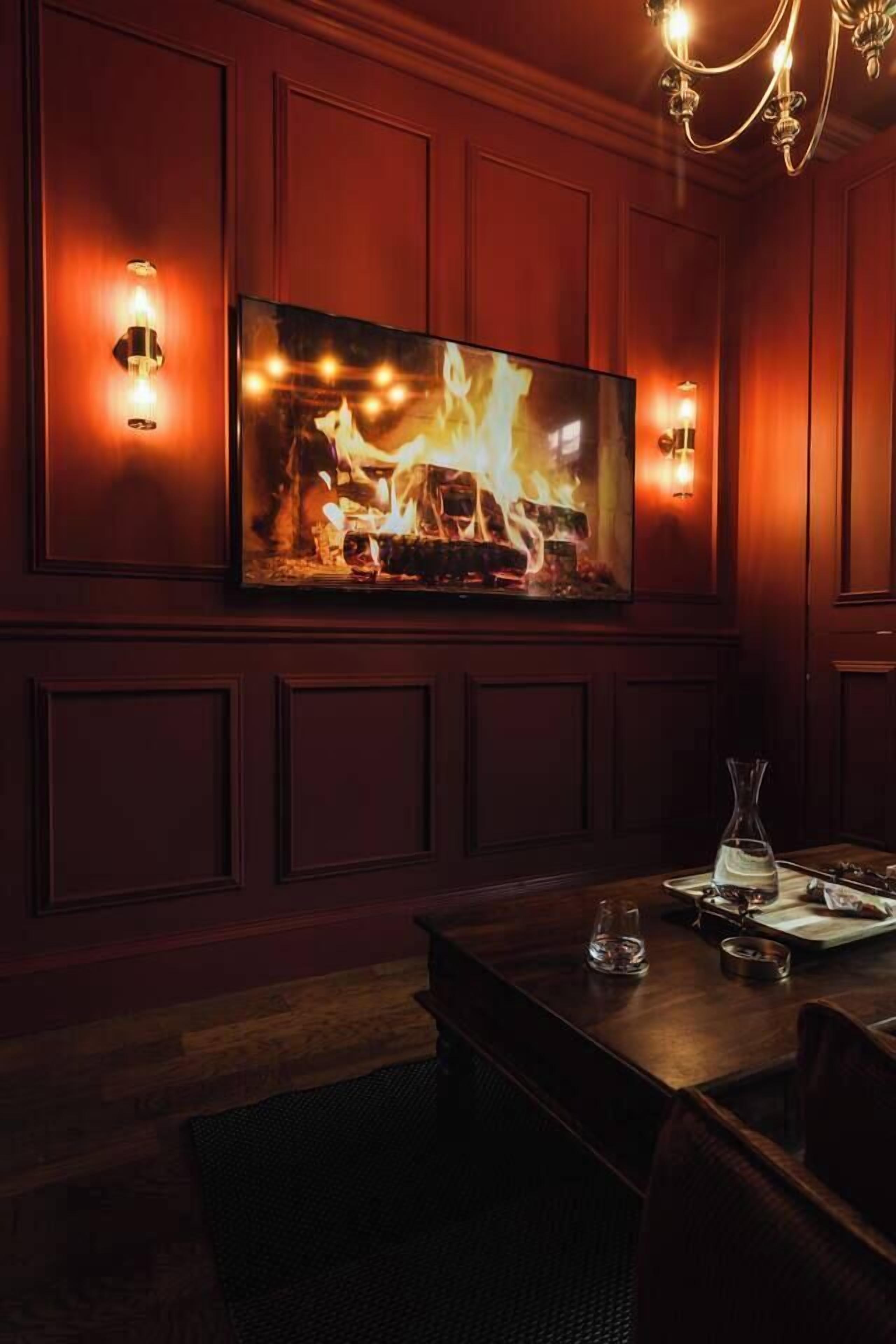 Un espace repas agrémenté d’un grand tableau représentant un feu, de lambris en bois et d’un lustre.