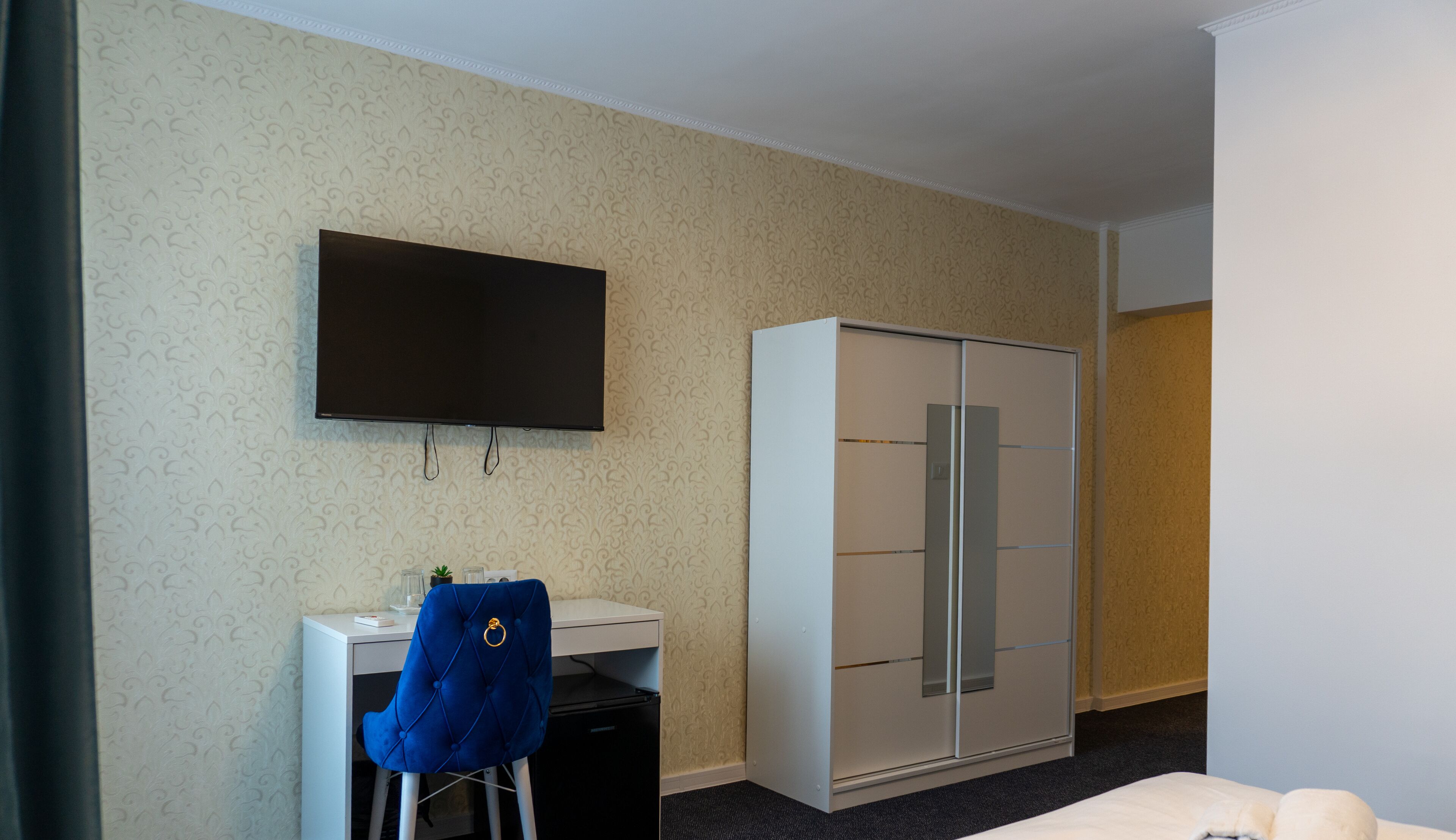 A hotel room with a bed, a desk with a chair, a television, and a wardrobe.