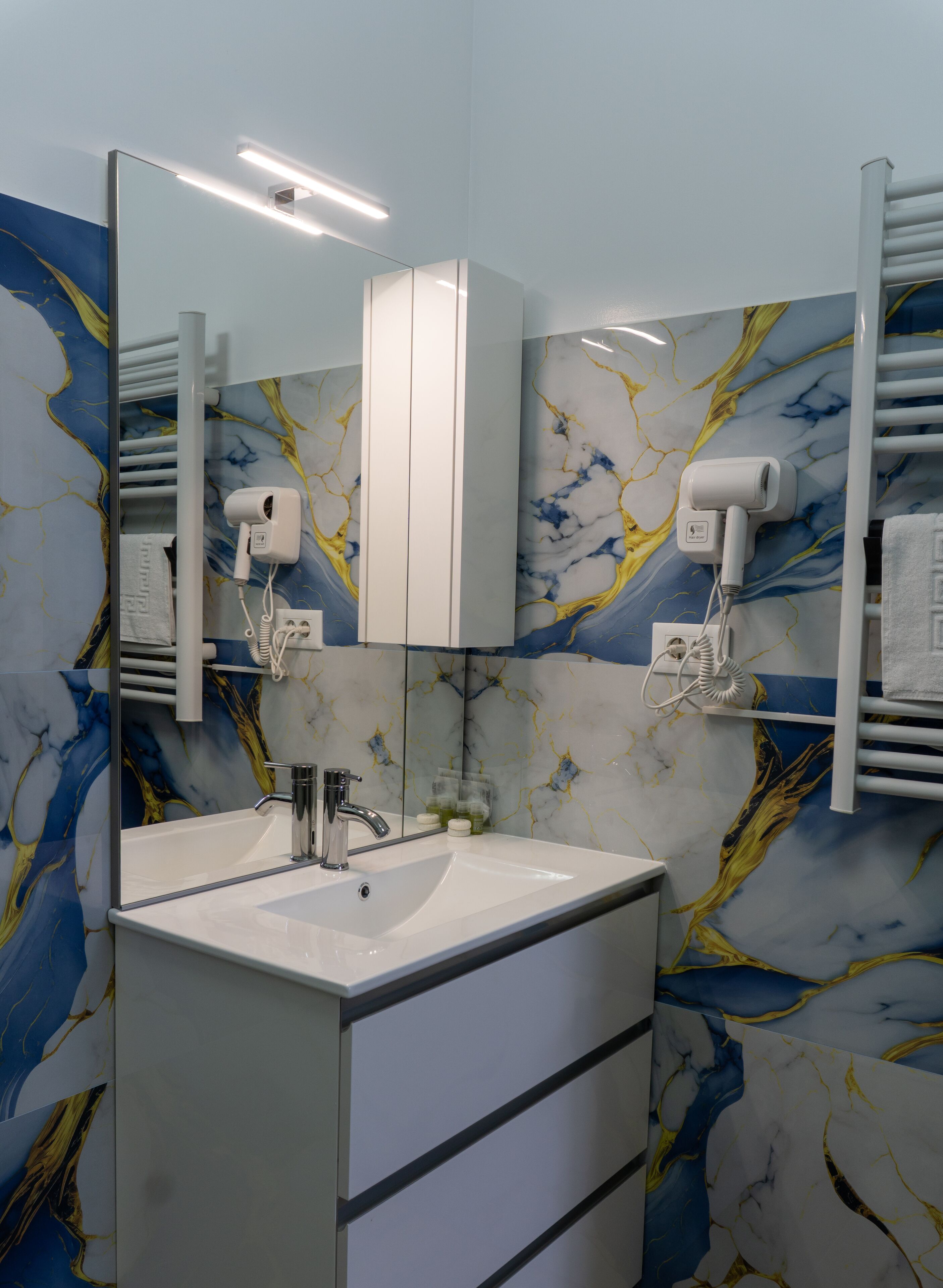 A bathroom with a white vanity, a mirror, a towel rack, and a hairdryer.
