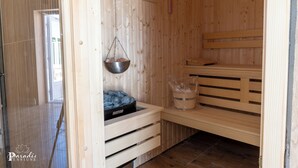 A sauna with wooden benches, a hanging metal basin, and a Harvia sauna heater. - Pensiunea Paradis Buzias (Buzias)