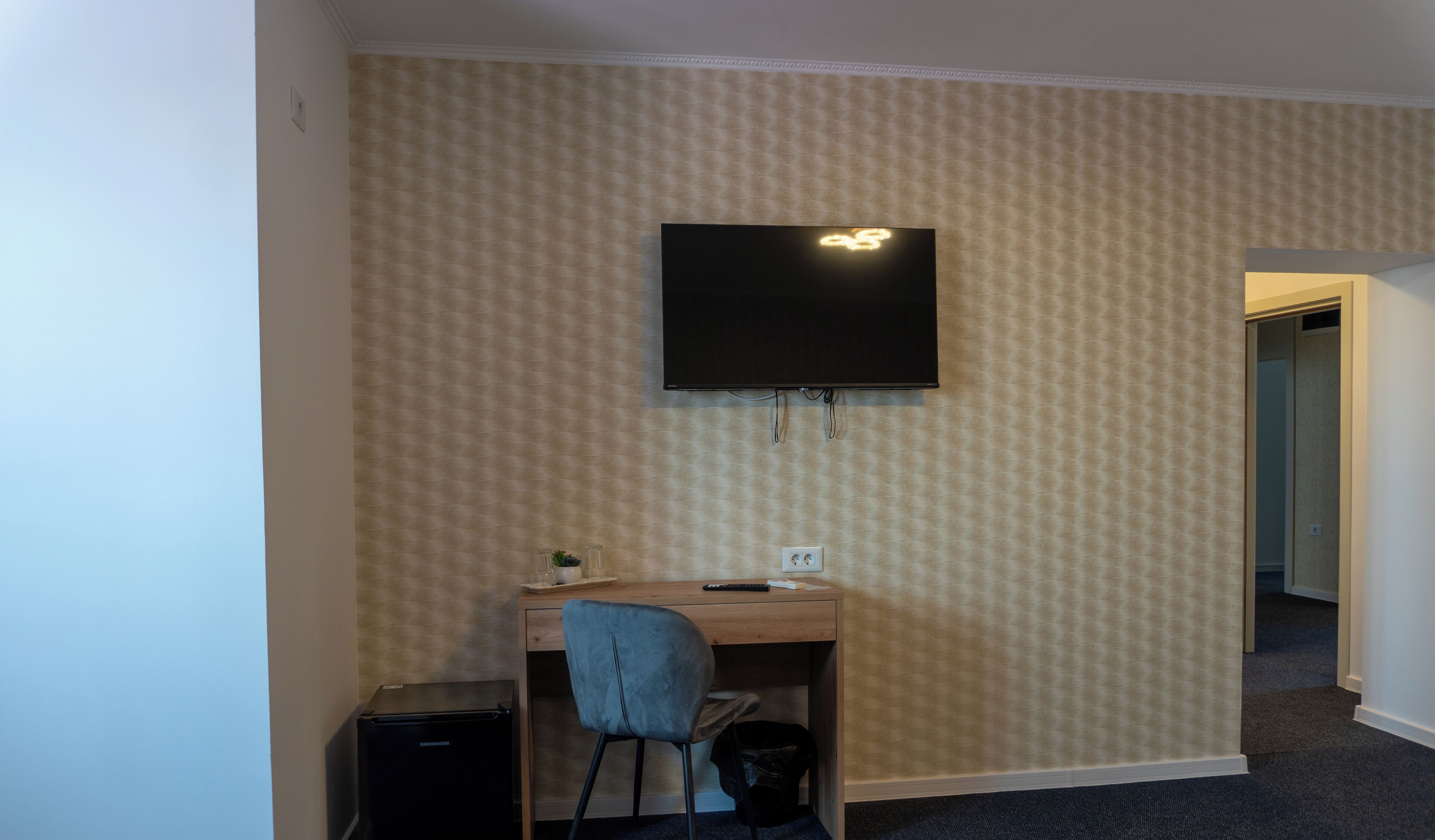 Una habitación pequeña con escritorio, silla y televisor montado en la pared.