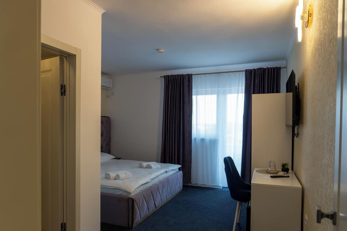 Ett hotellrum med en säng, ett skrivbord, en stol, en spegel och ett fönster med gardiner.