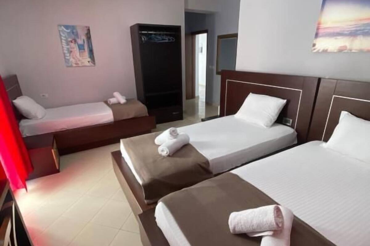 A hotel room with two beds, a wardrobe, a painting, and a red curtain.