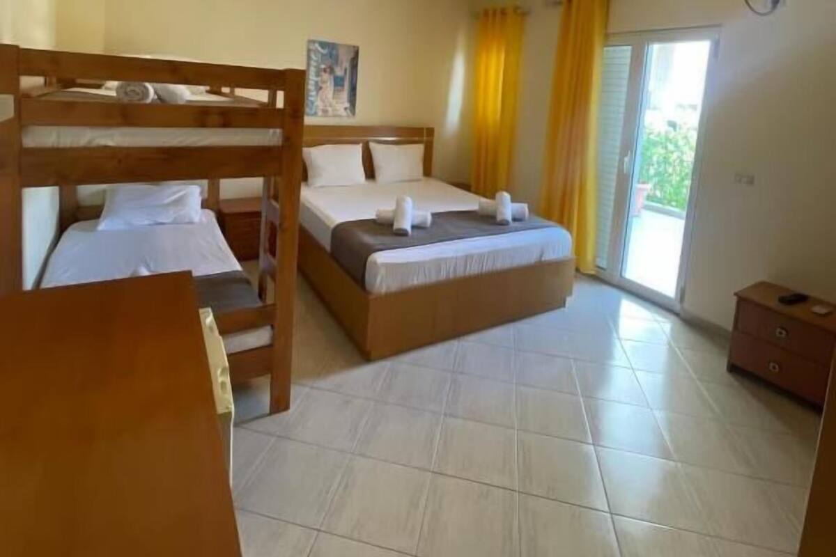 A hotel room with a bunk bed, a single bed, a wooden desk, and a small cabinet.